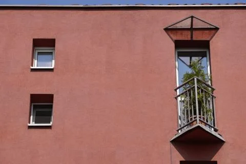 Small triangular balcony in the house with a coral facade and potted flowers  Stock Photos