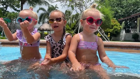 Small triplets sisters playing in the pool in swimsuits 库存影片 244007948