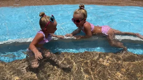 Small triplets sisters playing in the pool in swimsuits 库存影片 244008094