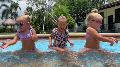 Small triplets sisters playing in the pool in swimsuits 库存影片 244008117