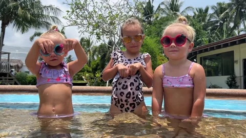 Small triplets sisters playing in the pool in swimsuits 库存影片 244008284