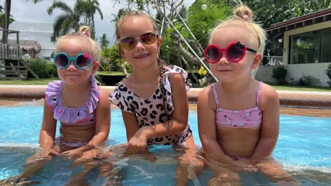 Small triplets sisters playing in the pool in swimsuits 库存影片 244008314