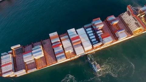 A small tug pushes a large sea freighter with containers creating spiral waves Video stock 129613761
