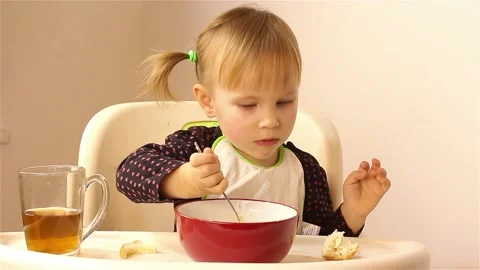 A small two-year-old girl eats porridge. Vídeos de archivo 87613086