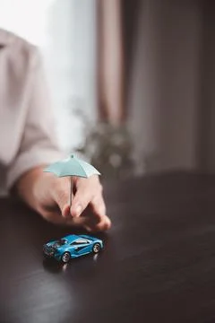 Small umbrella held above a blue car model symbolizes vehicle insurance, ac.. Stock Photos