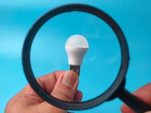 A small USB LED light bulb held in a hand is focused on through a magnifyin.. 库存照片