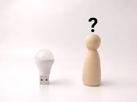 A small USB light bulb device sits next to a wooden peg doll beneath a blac.. Stock Photos