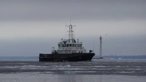 A small vessel sails against background of a lighthouse. Ice on the water. Boat Stock Footage 148349393