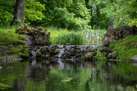 Small water cascade made of arranged stones in a shady green park Фото