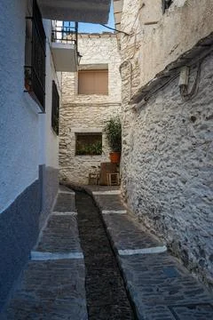 A small water stream flowing through a narrow alley of white buildings under  Stock Photos