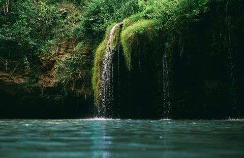 A small waterfall and a lake surrounded by trees in the summer. Wonderful lan Stock Photos