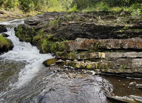 Small waterfall and layered rock formation in a forest. Stock Photos