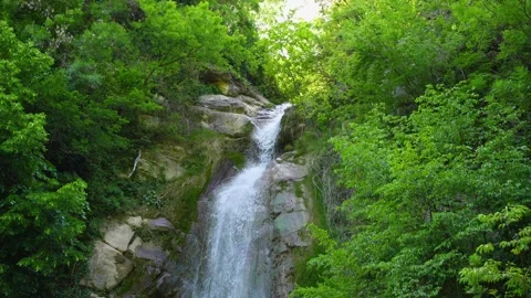 Small waterfall cascading down rocky cliff face. Flowing water in environment Stock Footage 319792332