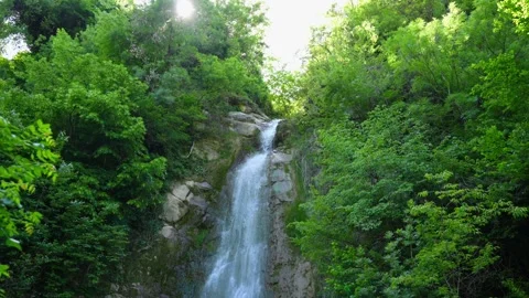 Small waterfall cascading down rocky cliff face. Flowing water in environment Stock Footage 319792350