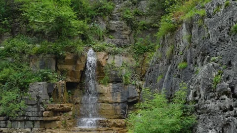 Small Waterfall Cascading Down Rocky Cliffside in Lush Green Forest Landscape Stock Footage 342310241
