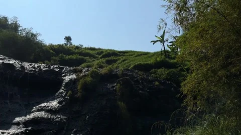 Small Waterfall Cascading Over Rocks, Lush Green Hillside, Clear Sky, Pan Down 스톡 동영상 324769705