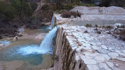 Small Waterfall Cascading Over a Stone Wall into a River Pond Stock Footage 305235726