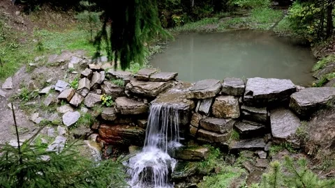 A small waterfall cascading into a pond in a green forest aerial view Stock Footage 308746128