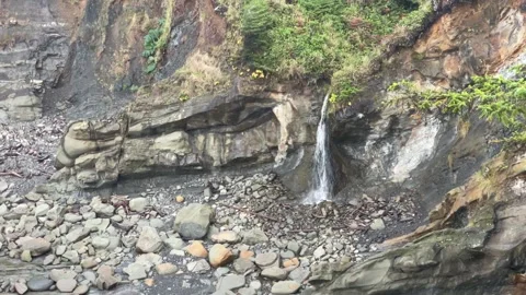 Small waterfall drops off a cliff to a rocky beach Video stock 329448836
