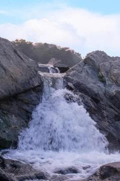 A small waterfall failing down between the rocks downhill Stock Photos