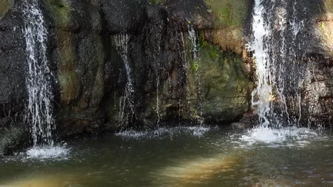 Small waterfall flowing over moss-covered rocks, creating a refreshing natural Stock Footage 329819787