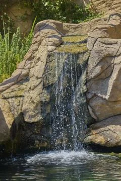 Small waterfall flowing over natural rocks into clear pond Fotos Stock
