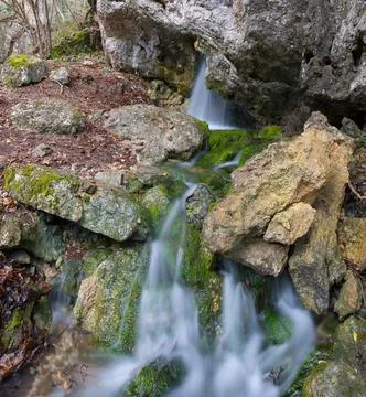 Small Waterfall Flowing Through Mossy Rocks in a Forest 스톡 사진