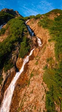 A small waterfall flows down the slope of a rock against a beautiful blue sky Stock Photos