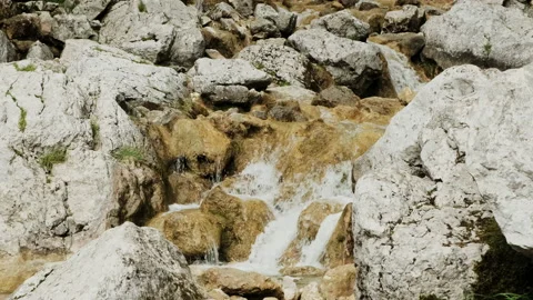 Small waterfall flows over white and colourful rocks in slow motion Stock Footage 136420832