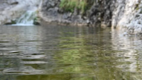 A small waterfall flows into a pool of a mountain river and creates waves (slow) Видео 212735521