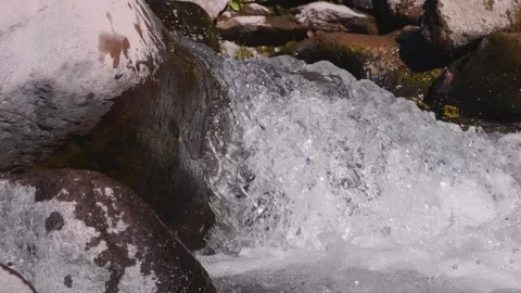 A small waterfall of a mountain stream with clear water flowing over rocks in th Video stock 320856725