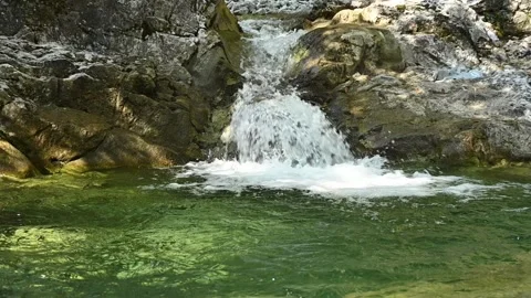 A small waterfall from a mountain stream runs into its pool (slow motion) Stock-Footage 260844088