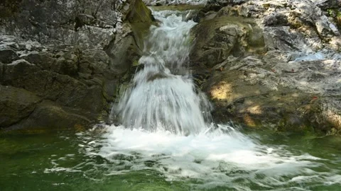 A small waterfall from a mountain stream runs into its pool Video stock 260844264