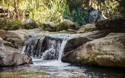 Small waterfall or river cascade - water flowing over large stones, sunlit .. Stock Photos