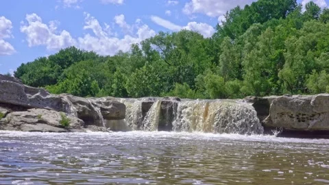 Small waterfall shot at low angle with green trees and blue sky Video stock 142397613