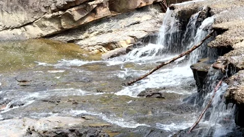 A small waterfall splashes onto a rocky creek bed in a mountain valley, 4k Stock Footage 337434855