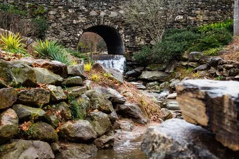 A small waterfall with a stream next to a stone wall Stock Photos