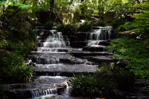 Small waterfall streaming down black rocks in japanese garden. Stock Photos