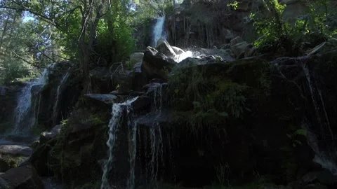 Small Waterfalls Flowing Over Dark Rocks with Sun Shining Through Stock Footage 232050502