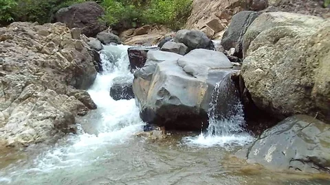 Small waterfalls stream through black and brown rocks on big river Stock Footage 125121691