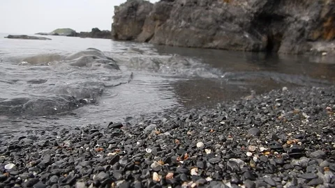Small waves of the calm sea lapping the black shore of the volcanic cliff Stock Footage 103425543