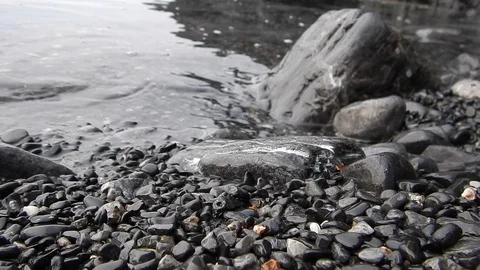 Small waves of the calm sea lapping the black shore of the volcanic cliff Stock Footage 103425721