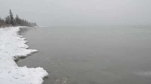 Small waves on a cold looking partially frozen lake as light snow falls on a Stock Footage 340240171
