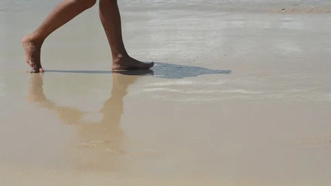 Small waves crash against shore. Along the sea, there are male feet on the sand Stock Footage