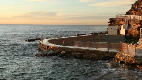 Small waves crash into empty rock pool during sunrise Stock Footage 90936785