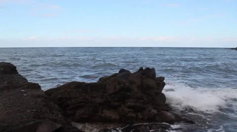 Small waves hitting against dark rock, blue sky with some scattered clouds Stock Footage 42743720