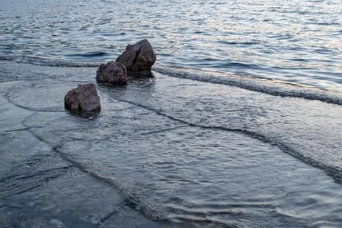 Small waves hitting beach with rocks in sunset Stock Photos