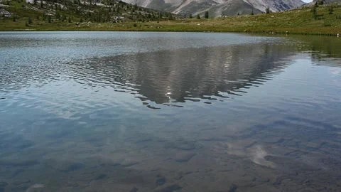 Small waves ripple across a mountain lake with a mountain reflecting in the Stock Footage 328428124