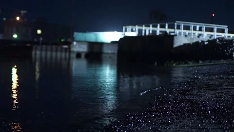 Small waves rippling on pebble beach at night with warehouse in background Stock Footage 233469357