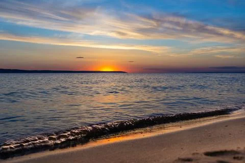 Small waves roll ashore, the red sun sets behind a distant cape, selective fo Stock Photos